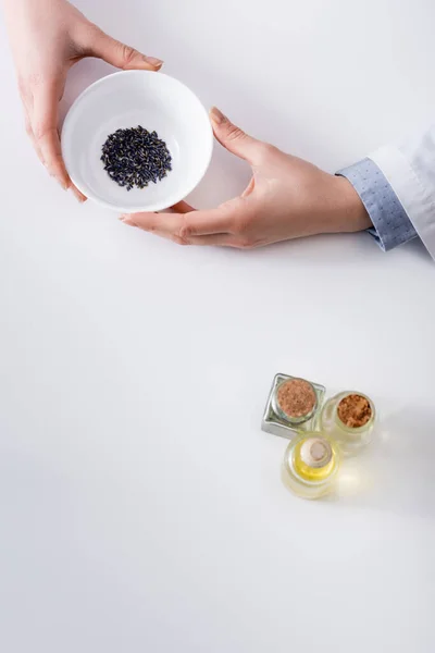 Vista superior de la mujer sosteniendo un tazón con lavanda seca mientras hace cosméticos - foto de stock