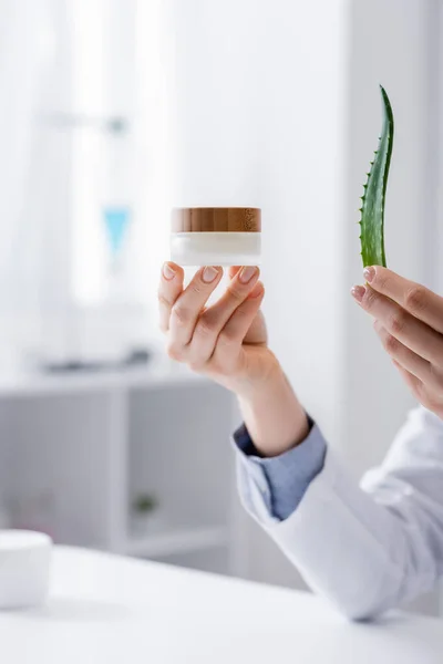 Partial view of laboratory assistant holding aloe and container with cream in lab — Stock Photo