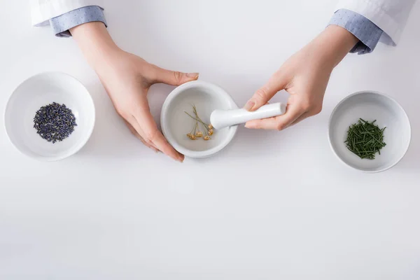 Top view of woman grinding dried flowers in mortar with pestle on white — Stock Photo