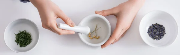 Top view of woman grinding dried flowers in mortar with pestle on white, banner — Stock Photo