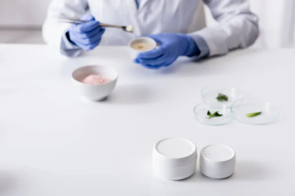 Containers with cream near blurred laboratory assistant in latex gloves — Stock Photo