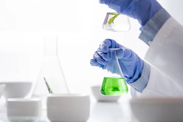 Cropped view of laboratory assistant in latex gloves holding flasks with green liquid — Stock Photo