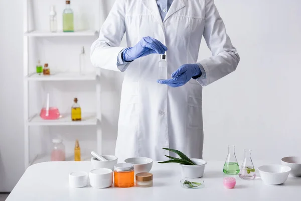 Обрезанный вид лаборанта в латексных перчатках с бутылкой сыворотки в лаборатории — стоковое фото