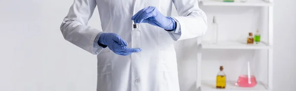 Vista recortada del asistente de laboratorio en guantes de látex sosteniendo botella con suero en laboratorio, pancarta - foto de stock