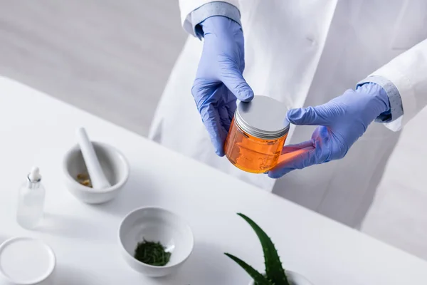 Vista en ángulo alto del asistente de laboratorio en guantes de látex sosteniendo tarro con miel en laboratorio - foto de stock