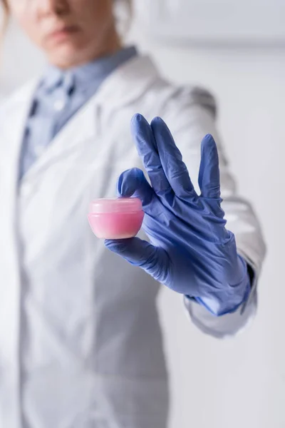 Cropped view of laboratory assistant in latex glove holding small container with cream — Stock Photo