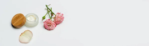 Rosa Blüten in der Nähe von Behälter mit Creme auf weiß, Banner — Stockfoto