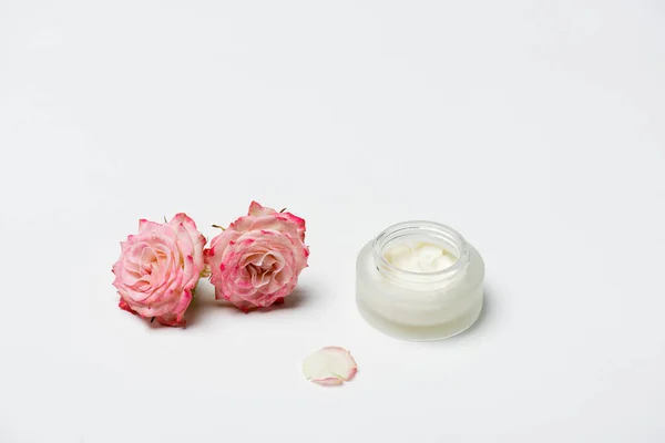 Rosa rosas perto de recipiente com creme em branco — Fotografia de Stock