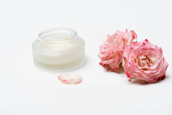 Primer plano de flores rosadas cerca de contenedor con crema sobre blanco - foto de stock