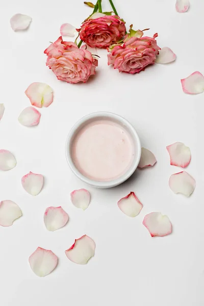 Vue du dessus des fleurs roses et des pétales près du bol avec crème sur blanc — Photo de stock