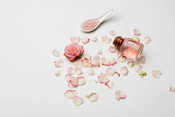 Vista de ángulo alto de rosa cerca de pétalos, sal de mar rosa y botella con agua de rosas en blanco - foto de stock