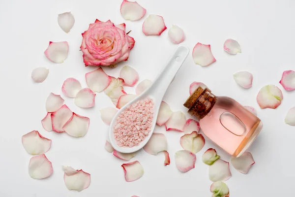 Вид зверху квітки біля пелюсток, рожева морська сіль і пляшка з трояндовою водою на білому — стокове фото