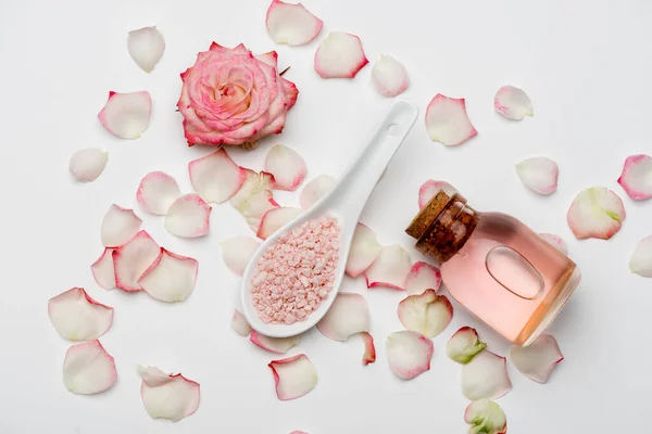 Vista superior de la flor cerca de pétalos, sal marina rosa y botella con agua de rosas en blanco - foto de stock