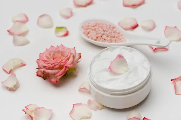 Flor cerca de pétalos, sal marina rosa y recipiente con crema sobre blanco — Stock Photo