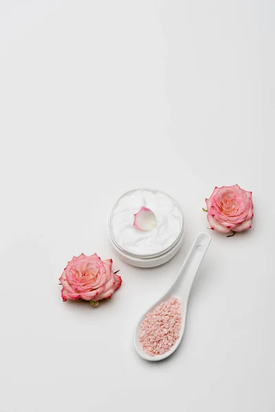 Вид зверху на квіти біля рожевої морської солі і контейнер з кремом на білому — стокове фото