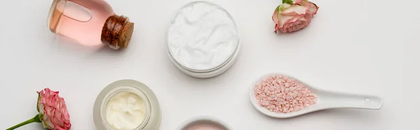 Vue du dessus des fleurs près du sel de mer rose, bouteille d'eau de rose et récipients avec crème sur blanc, bannière — Photo de stock