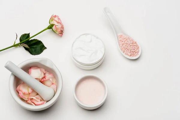 Vista superior da flor perto de sal marinho rosa, recipiente com creme, pilão e argamassa com pétalas em branco — Fotografia de Stock