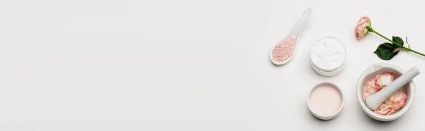 Top view of flower near pink sea salt, containers with cream, pestle and mortar with petals on white, banner — Stock Photo