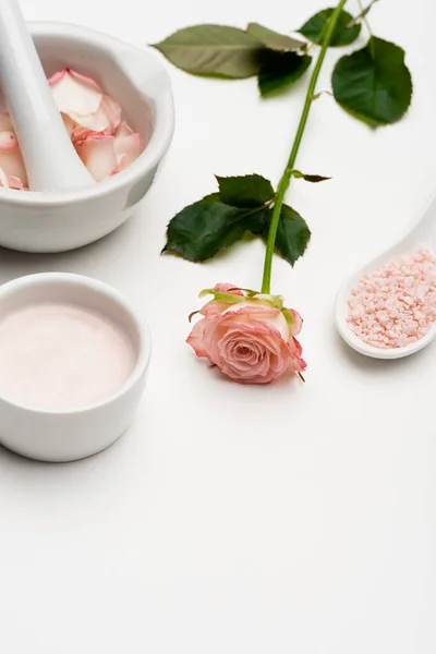 Flor cerca de la sal marina rosa, tazón con crema, mortero y mortero con pétalos en blanco - foto de stock