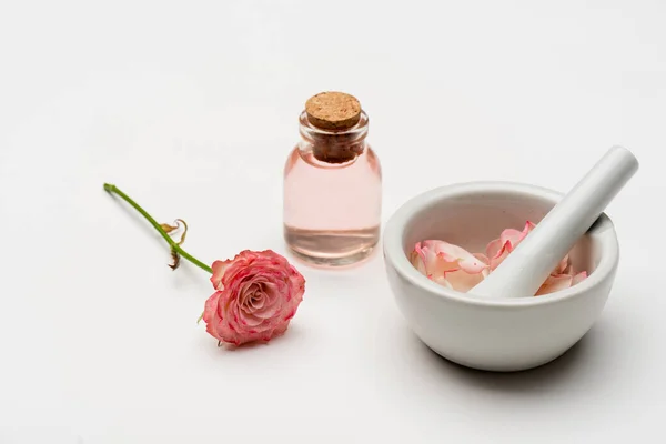 Fiore vicino pestello e malta con petali e bottiglia con acqua di rose su bianco — Foto stock