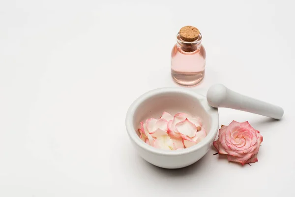 Flor perto de pilão e argamassa com pétalas e garrafa com água rosa sobre branco — Fotografia de Stock