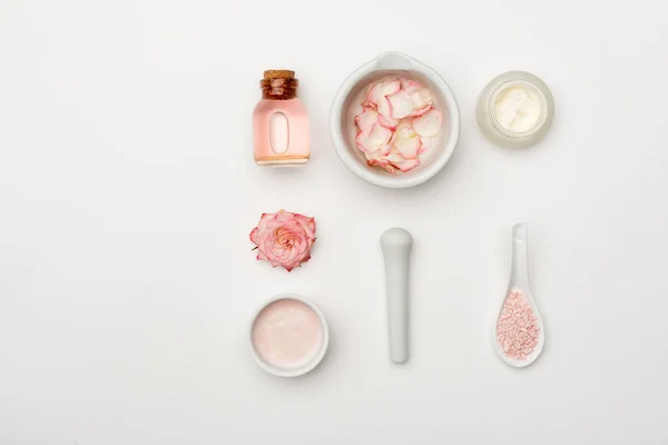 Top view of flower near pestle and mortar with petals, sea salt, cream and bottle with rose water on white — Stock Photo