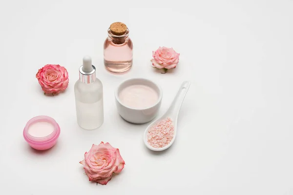 Flores cerca de la sal marina, suero y botella con agua de rosas en blanco — Stock Photo