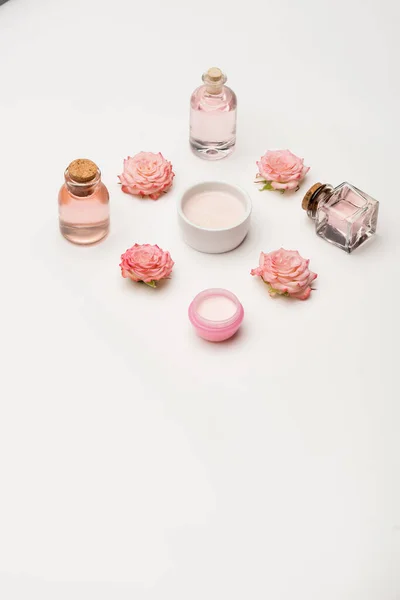 Colocação plana de flores perto de creme e garrafas com produtos cosméticos em branco — Fotografia de Stock