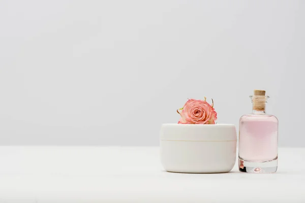 Bottle with extract near container with cream and pink flower on white — Stock Photo