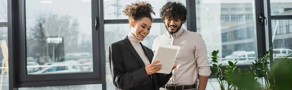 Negocio afroamericano positivo usando tableta digital cerca de colega indio en la oficina, bandera - foto de stock