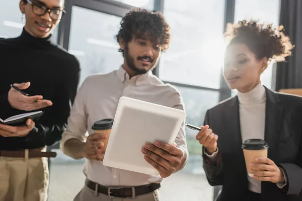 Digital tablet in hand of blurred indian businessman near african american colleagues in office — Stock Photo