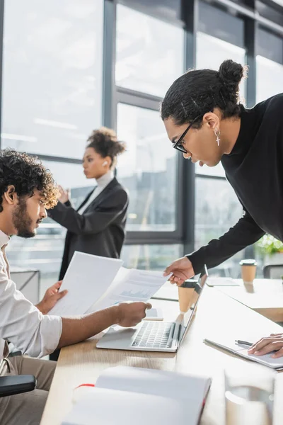 Side view of multiethnic businessmen working with papers near devices in office — Stock Photo