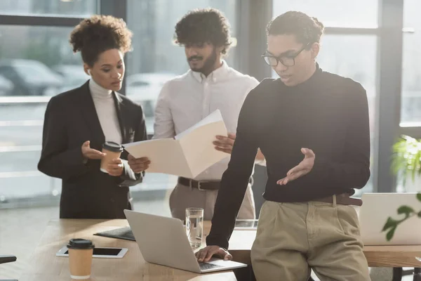 Joven hombre de negocios afroamericano teniendo video chat en el ordenador portátil cerca de colegas interracial en la oficina — Stock Photo