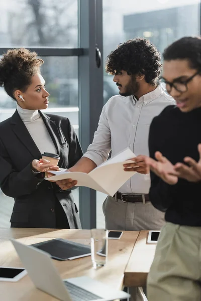 Des hommes d'affaires multiethniques travaillant avec des journaux à proximité d'appareils et un collègue afro-américain au bureau — Photo de stock