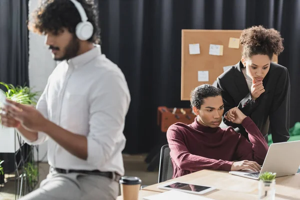 African american business people using laptop near blurred indian colleague in headphones in office — Stock Photo