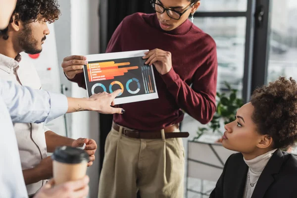 African american businessman holding paper with graphs near interracial colleagues in office — Stock Photo