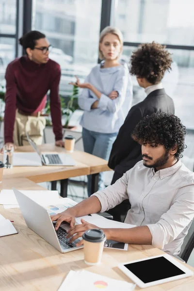 Uomo d'affari indiano che utilizza il computer portatile vicino al caffè per andare e documenti in ufficio — Foto stock