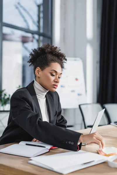 Donna d'affari afroamericana che prende appunti appiccicosi vicino a laptop e notebook in ufficio — Foto stock