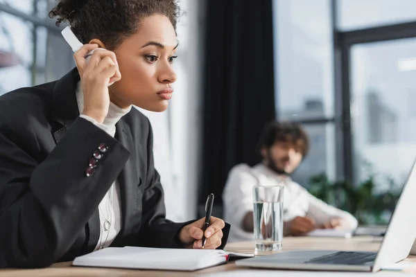 African american businesswoman in headphones writing on notebook near laptop in office — Stock Photo