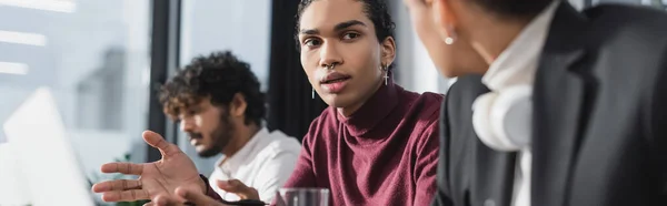 Afrikanischer Geschäftsmann zeigt mit Händen in der Nähe von Laptop und Amtskollegen, Banner — Stockfoto