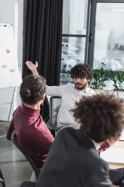 Empresário indiano apontando para flip chart perto de colegas afro-americanos no escritório — Fotografia de Stock