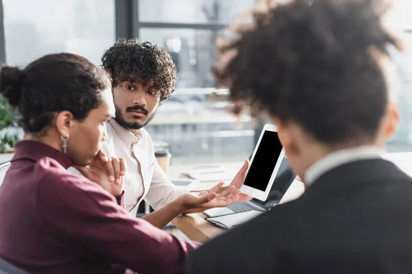 Empresario indio sosteniendo tableta digital cerca borrosa colegas afroamericanos en la oficina - foto de stock