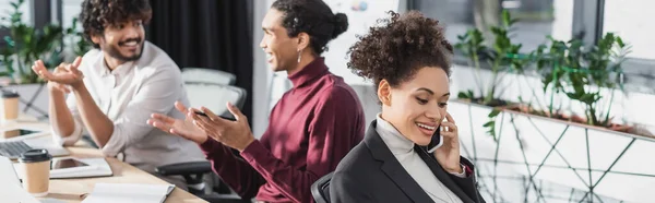 Cheerful african american businesswoman talking on cellphone in office, banner — Stock Photo