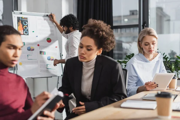 Empresaria usando tableta digital cerca de colegas interracial que trabajan en la oficina - foto de stock