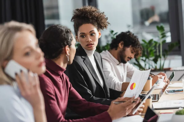 African american businesswoman holding paper near colleague with digital tablet in office — Stock Photo