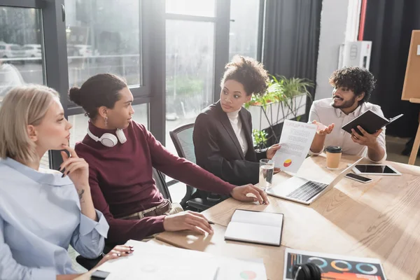 Multiethnic business people working with documents near devices on table in office — Stock Photo