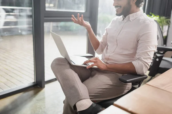 Ausgeschnittene Ansicht indischer Geschäftsmann lächelt während Videoanruf auf Laptop im Büro — Stockfoto