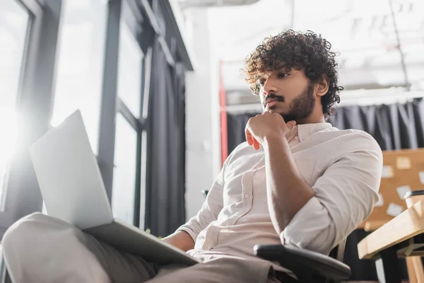 Visão de baixo ângulo do jovem empresário indiano usando laptop desfocado no escritório — Stock Photo