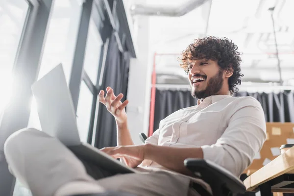 Vista de ángulo bajo de alegre empresario indio que tiene chat de vídeo en el ordenador portátil en la oficina - foto de stock