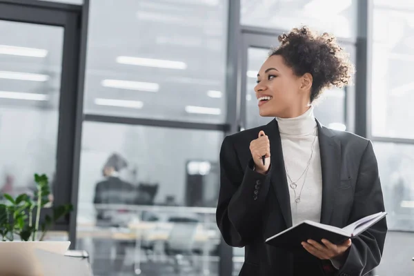 Positive african american businesswoman holding notebook in office — Stock Photo